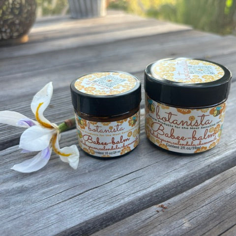Botanista Babee Balm two glass jars on wooden surface with orchid flower
